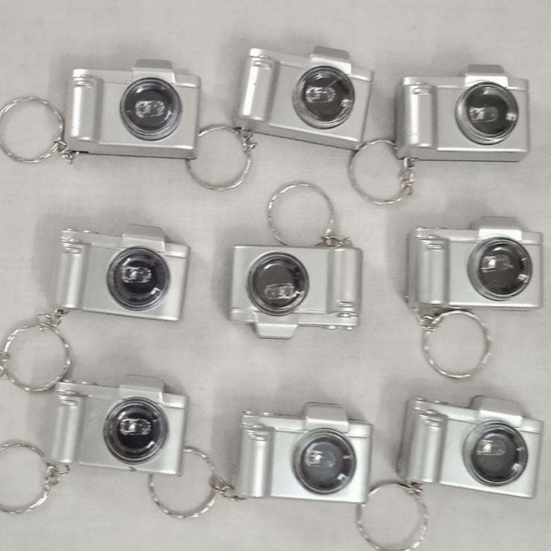 Silver camera-shaped keychains arranged in a grid on a light gray background
